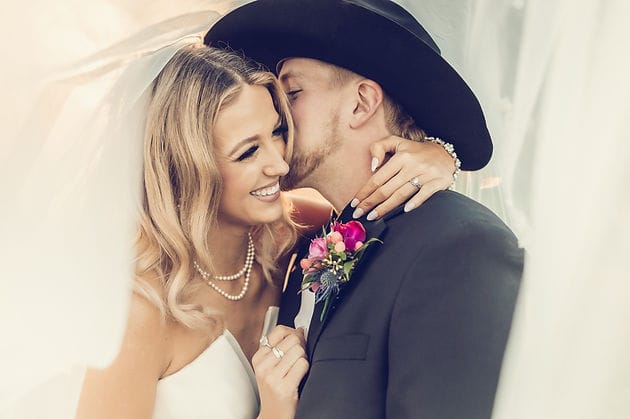 A bride and groom snuggle together under veil